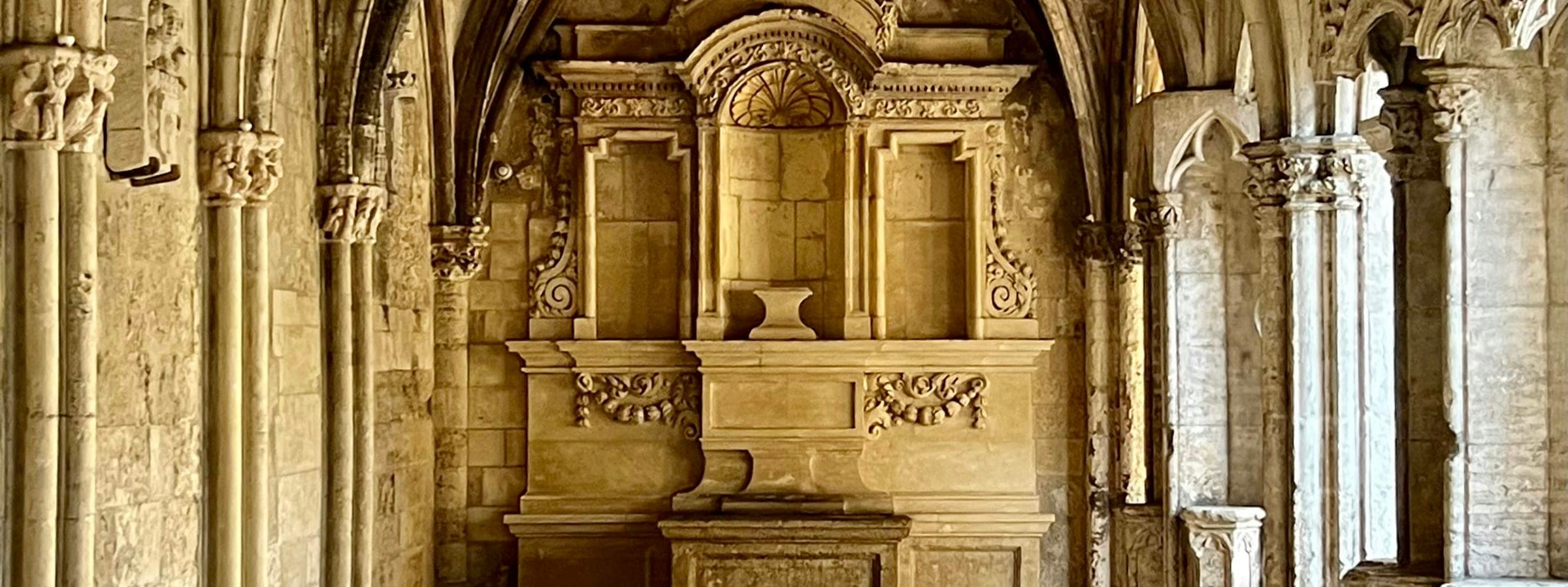 Carved stone columns, capitals and entablature of a church front, weathered and lit low from one side.