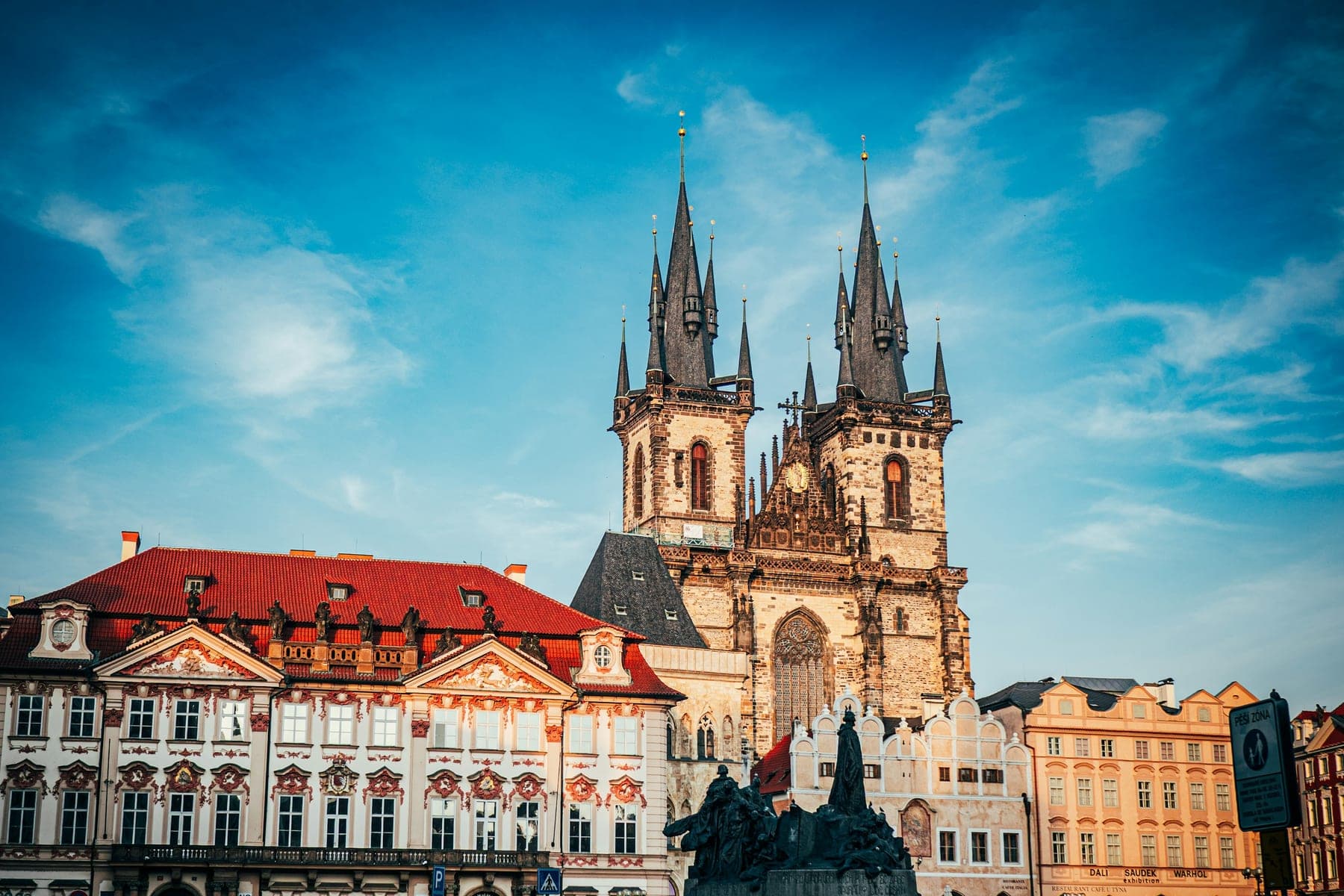 A terrace of baroque town houses along one side of a market square, the twin Gothic towers of a church rising behind their roofs.