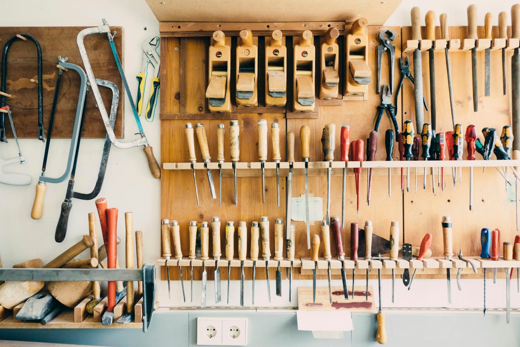 Hand tools hung in order on a workshop wall — saws, chisels and gouges ranged above the bench.